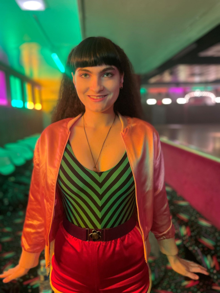 Ivy Wolk and Rhonda in The Shards with her hair cut in blunt bangs and wearing a pink bomber jacket and striped leotard.